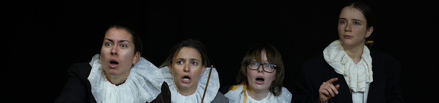 Szenenbild einer Theaterproduktion der Theaterakademie Stuttgart mit vier Schauspielerinnen auf dunkler Bühne